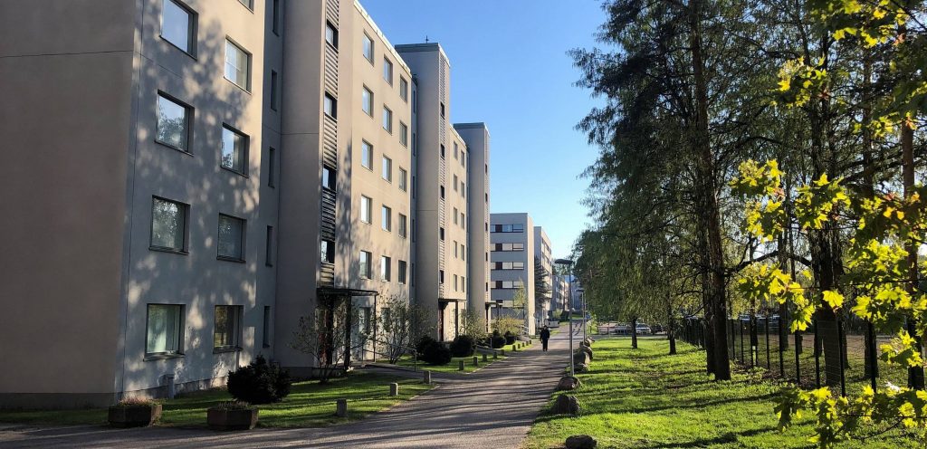 Grey apartment buildings next to a walking lane and a lush park in Runosmäki nieghborhood in Turku.