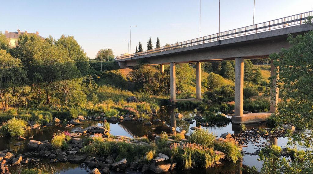 Halinen bridge close to the Halinen Dam goes above River Aura when the water level is low and many rocks can be seen on a green summer evening.