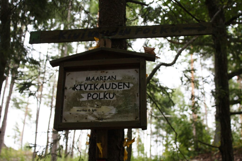 Metsän keskellä oleva puinen kyltti, jossa lukee "Maarian kivikauden polku. Matka 6 km".