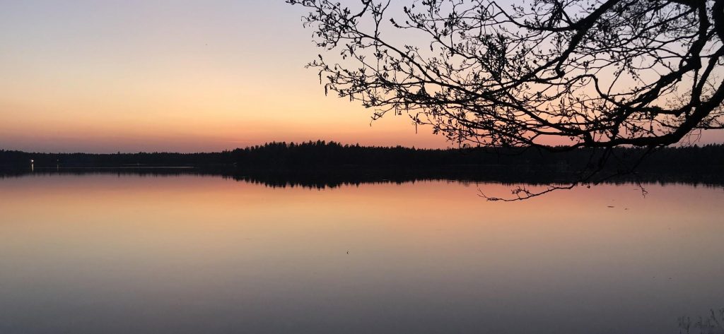 Littoistenjärvi auringonlaskun aikaan, jolloin taivas ja vesi ovat värjäytyneet oranssin ja violetin eri sävyihin.