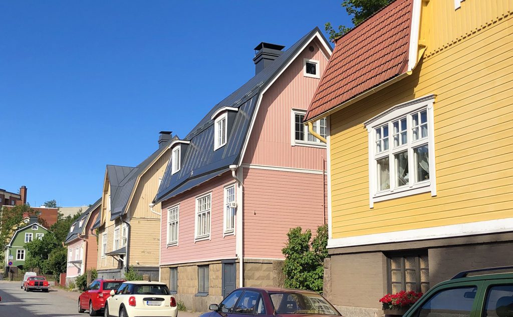 Yellow, pink, beige and green wooden houses in a row on a sunny day in the neighbourhood of Pohjola in Turku.