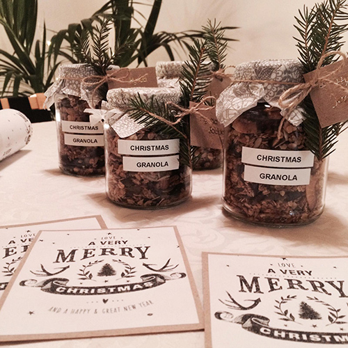 Christmas cards with a text 'a very merry christmas' together with glass jars filled with homemade granola.
