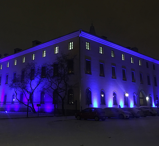 Rakennus, joka on valaistu siniseksi Suomen itsenäisyyspäivän kunniaksi. Maassa kevyt lumipeite.