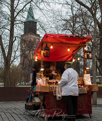 Handicraft stand at the Christmas market with a seller and a buyer. Turku Cathedral in the background.