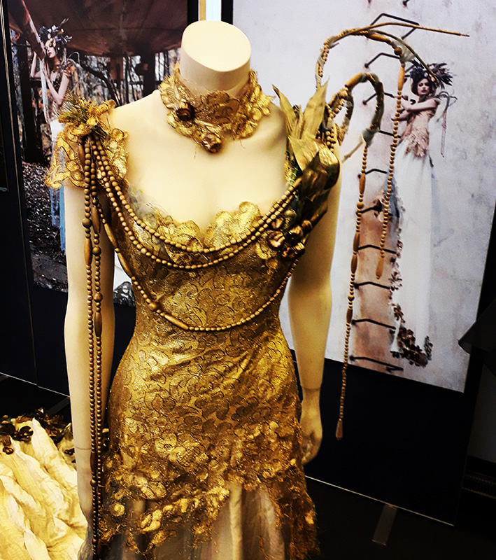 Kultainen koristeellinen mekko mallinuken päällä Turun kaupunginkirjaston näyttelyssä.