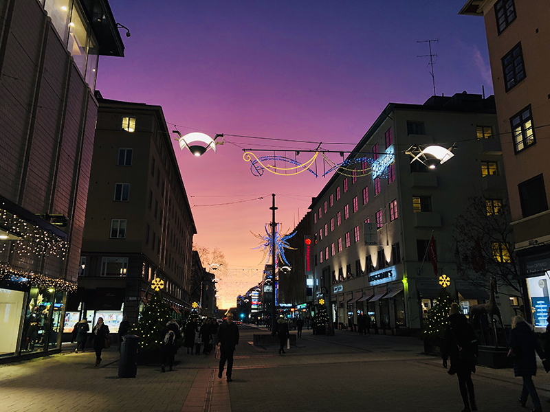 Turun keskustassa Yliopistonkadulla kävelee muutamia ihmisiä ja joulukoristeet roikkuvat kadun yllä taivaan hohtaessa väreissä. 