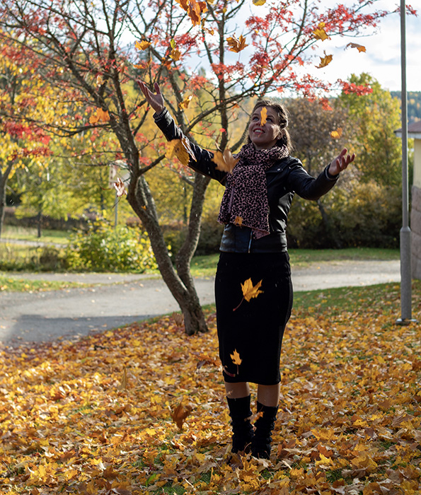 A girl with a leatherjacket and a skirt smiling and throwing autumn leaves to the air in Tuorla in Kaarina.