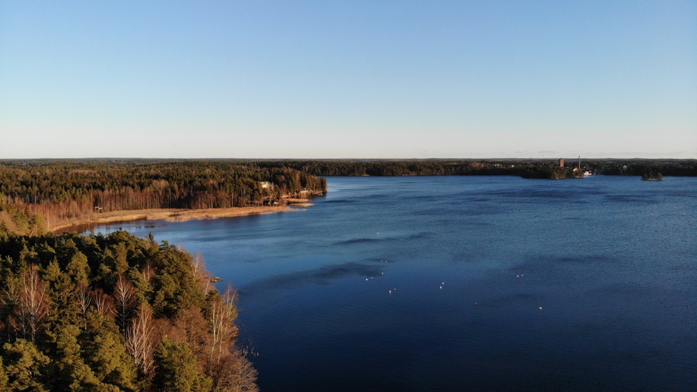 Littoistenjärvi ilman jäitä kuulaana tammikuun päivänä, järven ympärillä avautuvaa metsää ja muutamia rakennuksia.