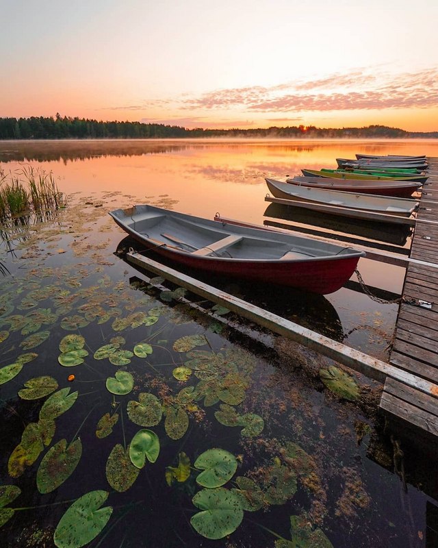 Soutuveneitä on kiinnitettynä laituriin ja kesäaamun aurinko värjää Littoistenjärven pinnan ja taivaan oranssiksi Kaarinassa.
