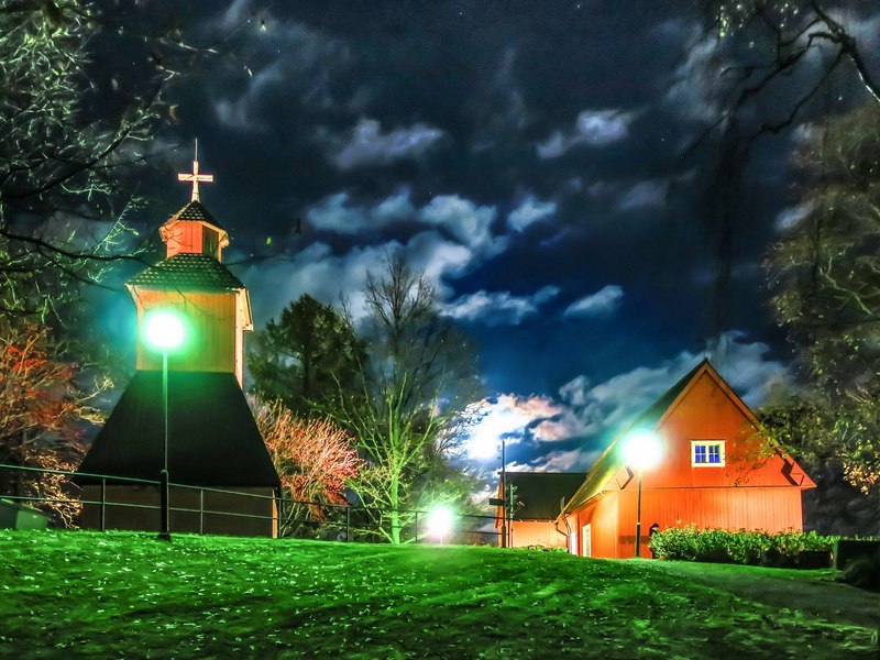 Kuusiston kirkko ja kaksi punaista puutaloa hohtaa maalauksen omaisesti yön pimeydessä Kuusiston saarella Kaarinassa.