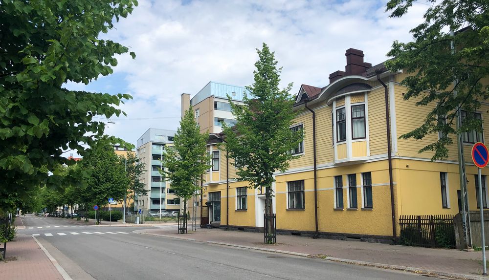 Yellow wooden row house by an asphalt street in the Eastern Center of Turku. 