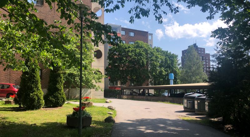 Aurinkoinen kesäpäivä Turun Varissuolla, jossa kohoaa tiiliverhoiltuja kerrostaloja rehevien puiden ympäröimänä.
