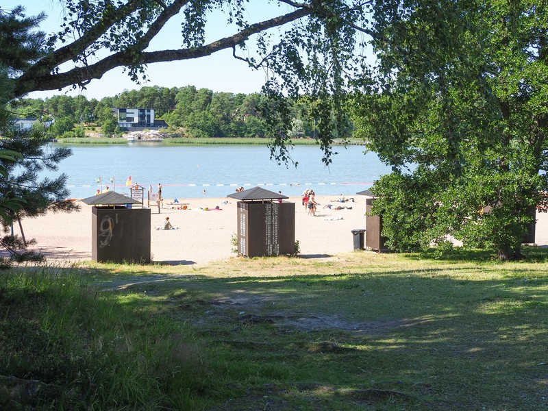 A lawn area, three changing rooms and a sandy beach on Turku's Ispoinen beach. The sea is in the background.