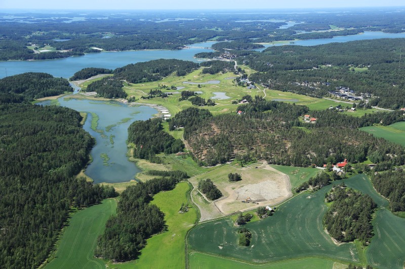 Aerial picture of the landscape of Luonnonmaa and the area where the new Housing Fair Area 2022 Lounatuuli will be built. There are woods, fields, patches of sea and a few houses.  