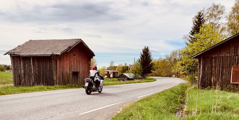 A motorcyclist on an asphalt road and old wooden barns.