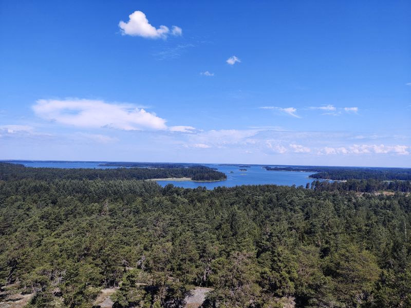 The view of the Houtskär island over the archipelago, evergreen forest in the front, bright ble sky and sea in the distance.