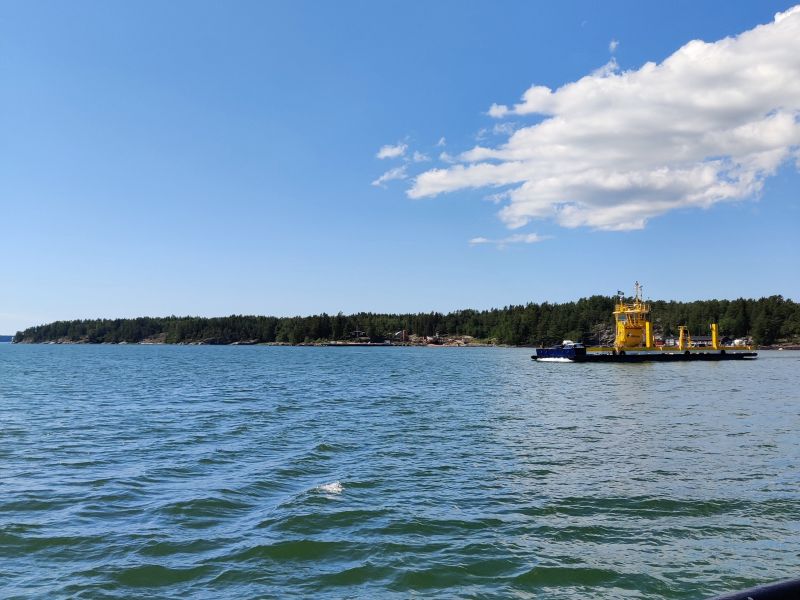 Pictured is the blue-green water, blue sky, and yellow Finnferries ferry connection on the archipelago road on the right. 