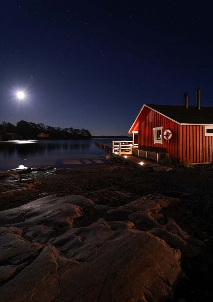 Bright moonlight lights a beach hut and a rocky beach in Kasnäs. 