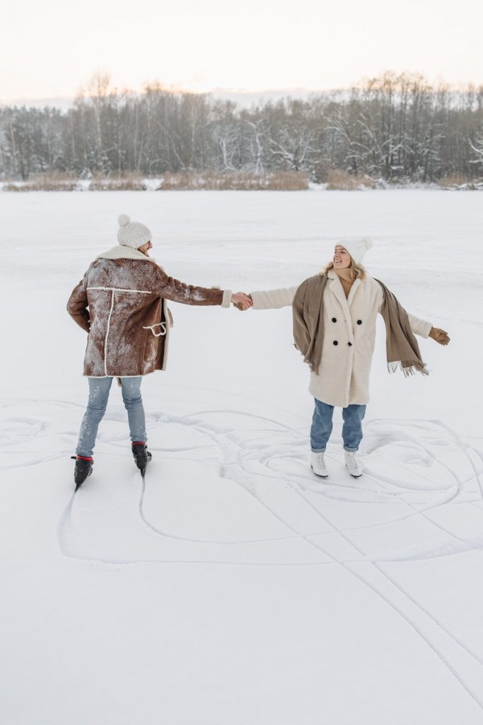 Mies ja nainen luistelevat kädestä kiinni pitäen lumisessa maisemassa.