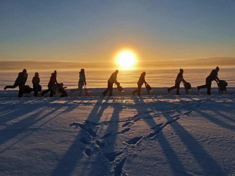 Potkukelkkailijoita Isojärven jäällä auringossa.