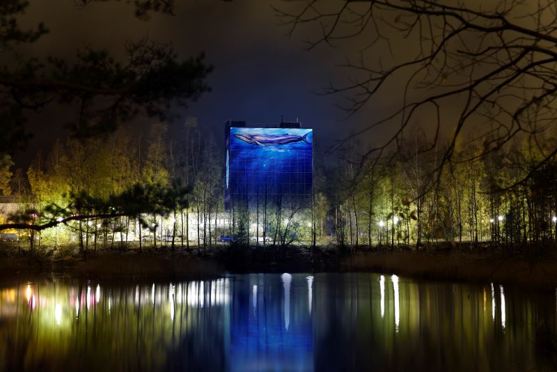 Valaistu korkea rakennus, jonka seinässä sinivalasta kuvaava taideteos