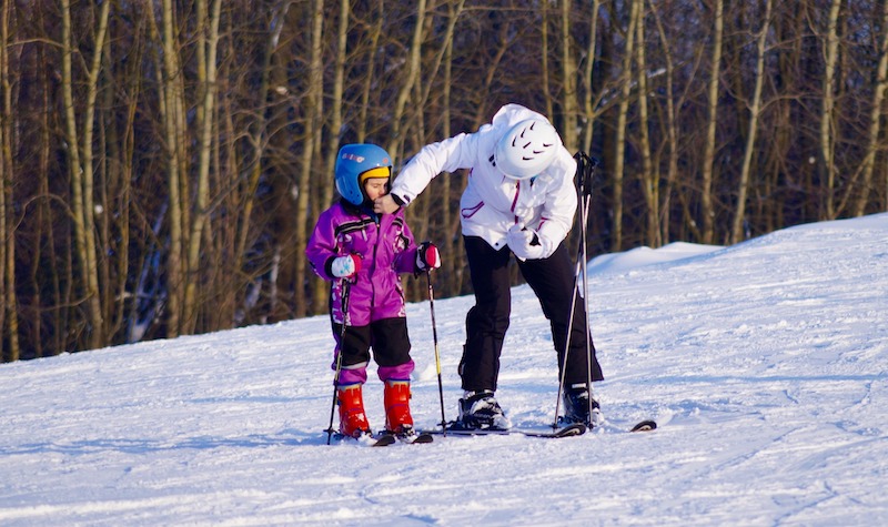 Aikuinen kiinnittää lapsen kypärää hiihtomäessä 