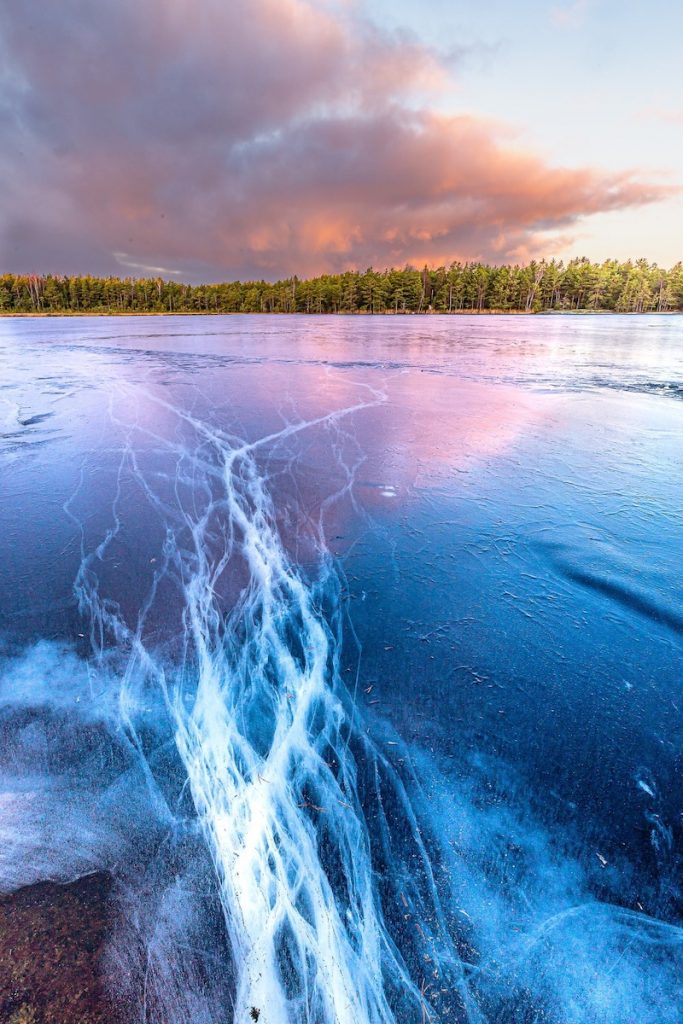 Kiermuraiset jäärailot jäätyneen järven jäällä Rymättylässä. Jäänpinta heijastaa taivaan pilvikuviot ja pastelliset sävyt.  