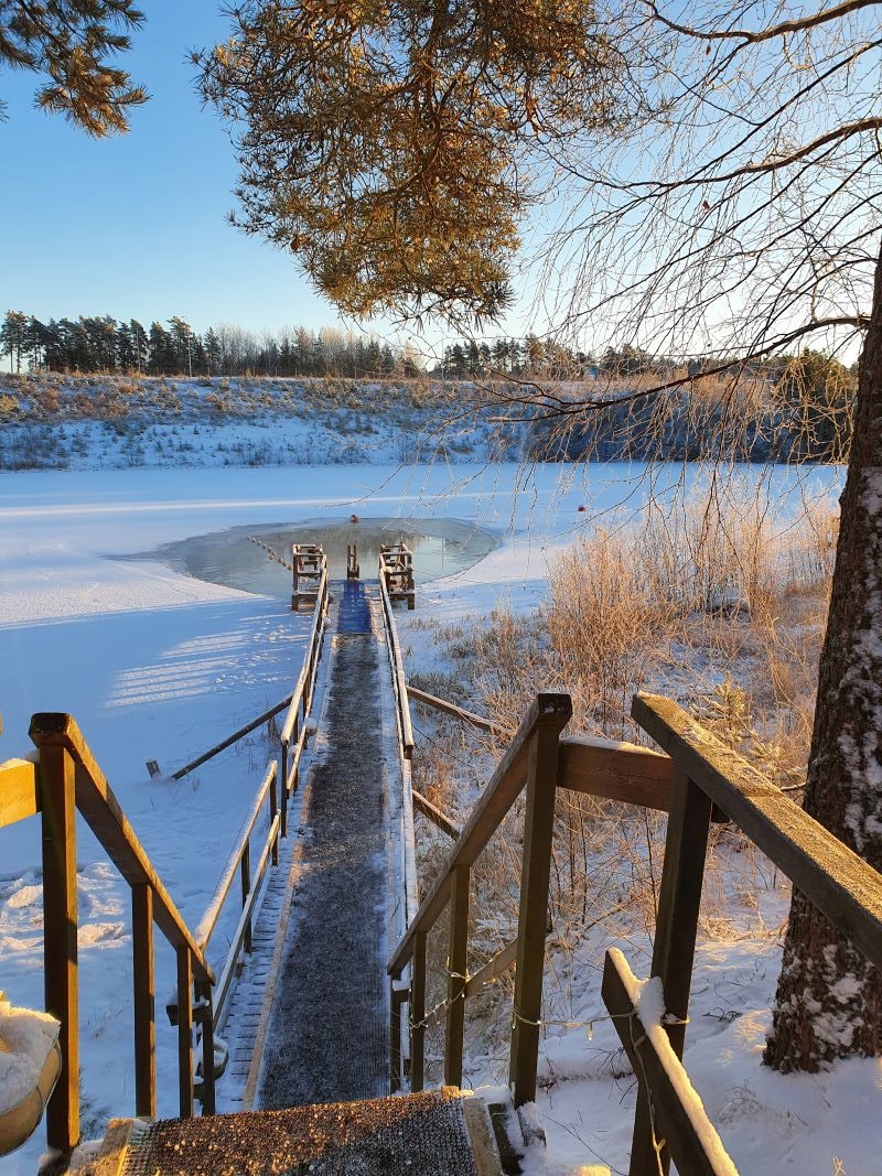 Kuvassa näkyy alas laskeutuva uimalaituri sekä sen päässä tikkaat avantoon talvisessa ja aurinkoisessa säässä. 
