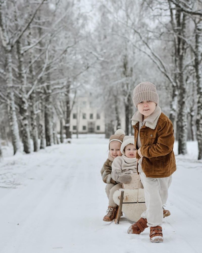 Lapsi vetää kahta lasta pulkassa talvisessa maisemassa ja takana näkyy Louhisaaren kartano.
