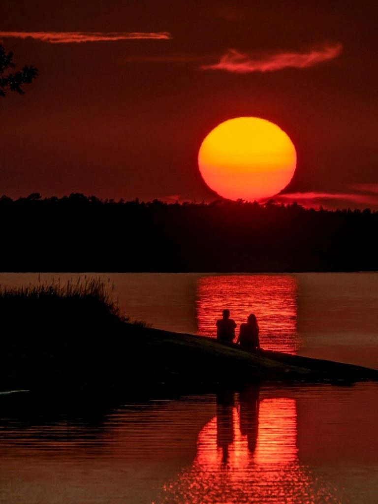 Kaksi ihmistä auringonlaskun aikaan rannalla.