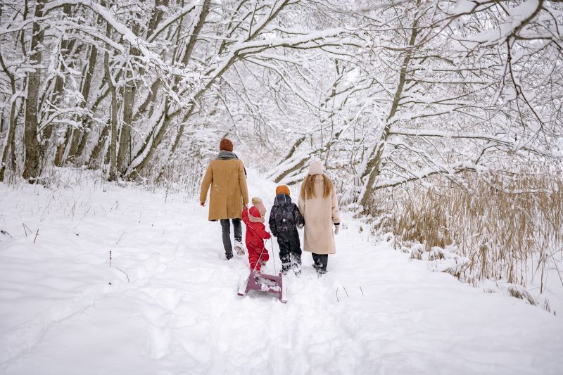 Perhe kävelee lumisessa maastossa ja vetää perässään pulkkaa.