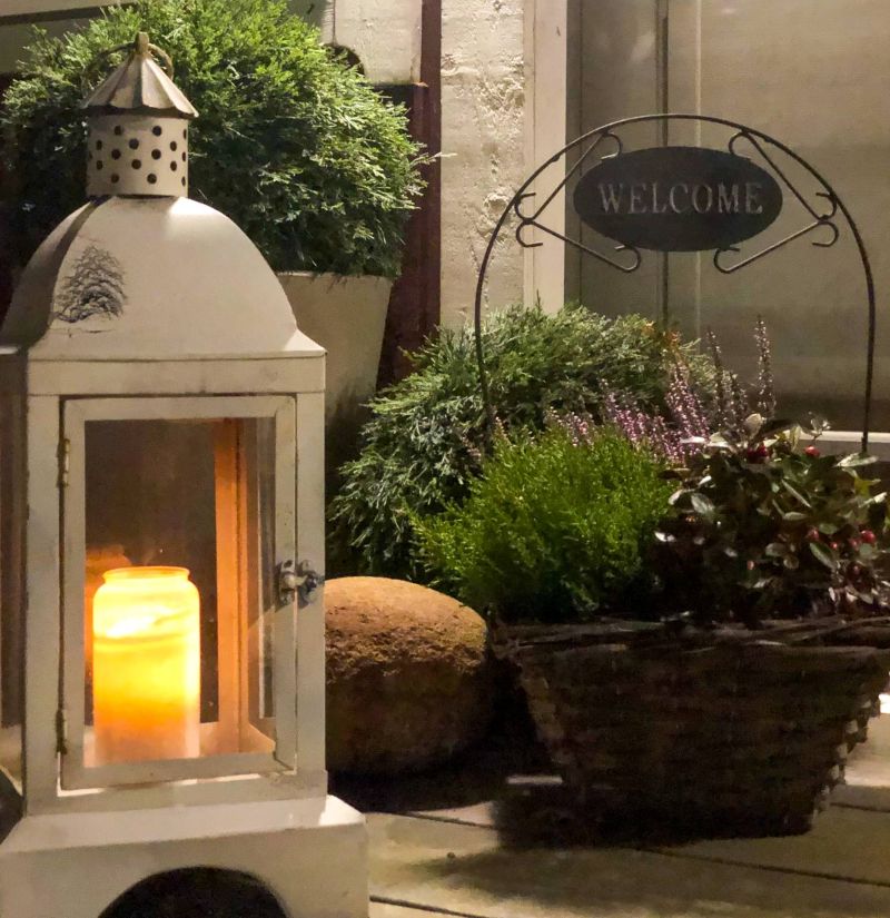 Kynttilälyhty ja kukkakori oven edessä.