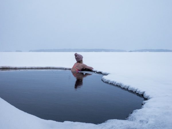Nainen nojaa järven reunaan ja katselee jäätynyttä järveä avannossa. 